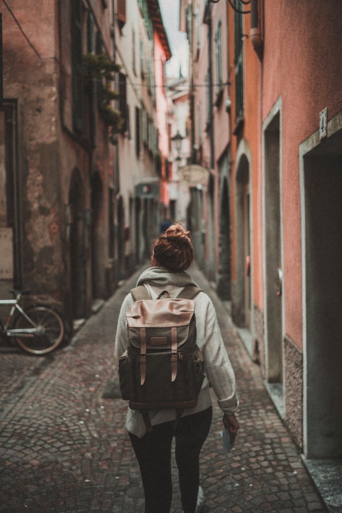 a person, with a backpack, facing away from the camera and into a narrow cobbled alleyway